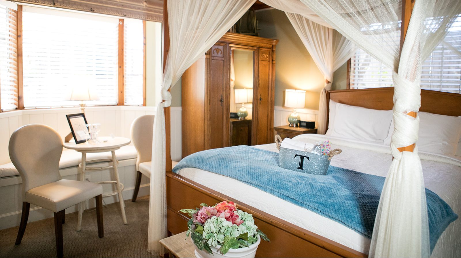 A cozy room with a four-poster bed, a small table and chairs, and a window.