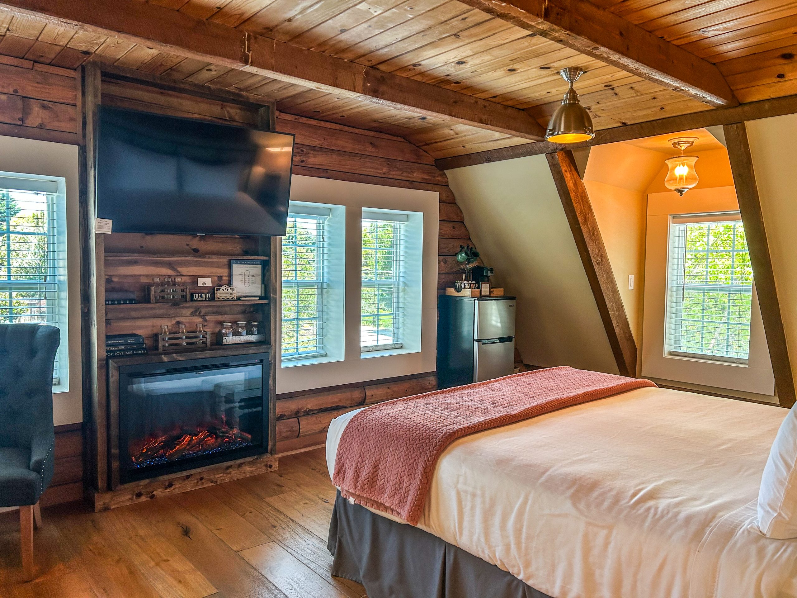 A wide view of a cozy room with a bed, fireplace, TV, and windows.